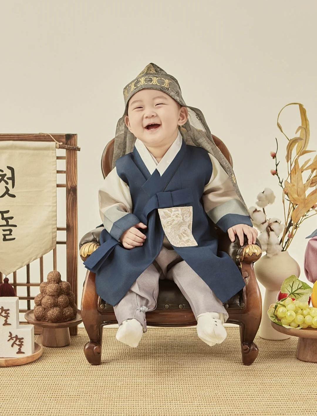 남색 한복에 호건을 쓰고 환하게 웃는 돌 아기 — 전통 돌상 돌사진