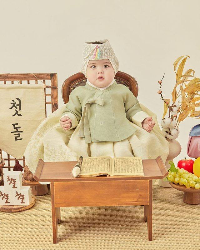 연둣빛 한복을 입고 서안 위 책과 붓 앞에 앉은 아기의 돌잡이 첫돌 돌사진