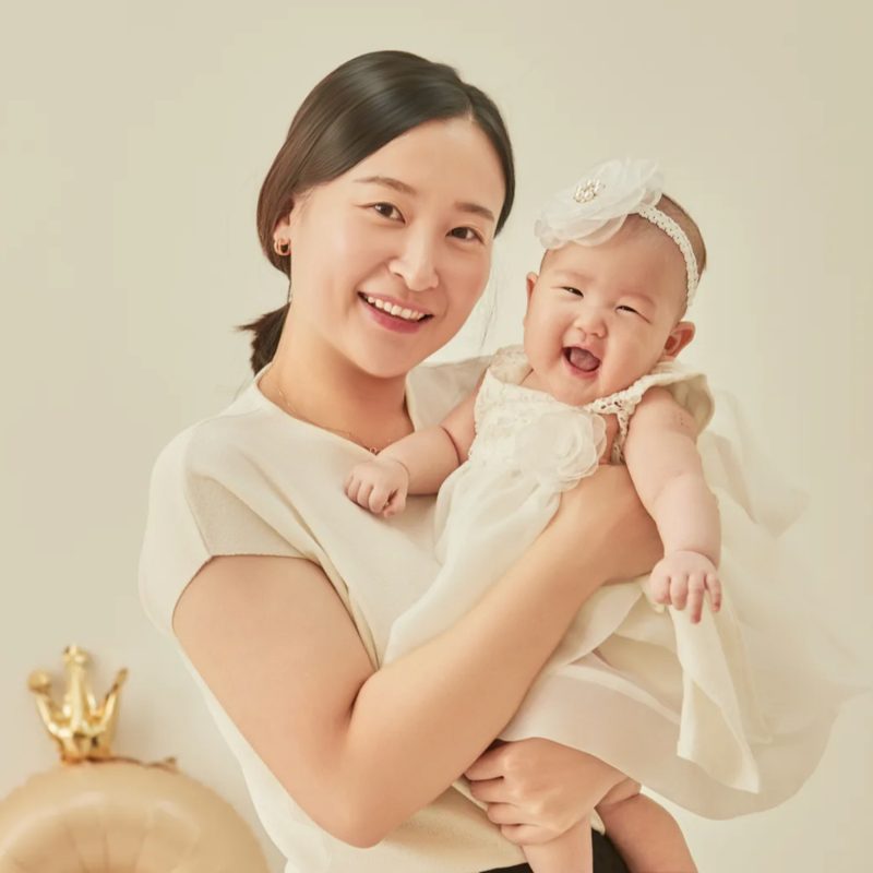 흰 드레스에 꽃 머리띠를 한 아기를 안고 함께 웃는 엄마와의 아기사진
